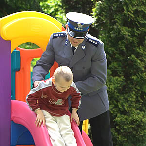 Na fotografii widać policjanta, który asekuruje chłopca zjeżdżającego na zjeżdżalni