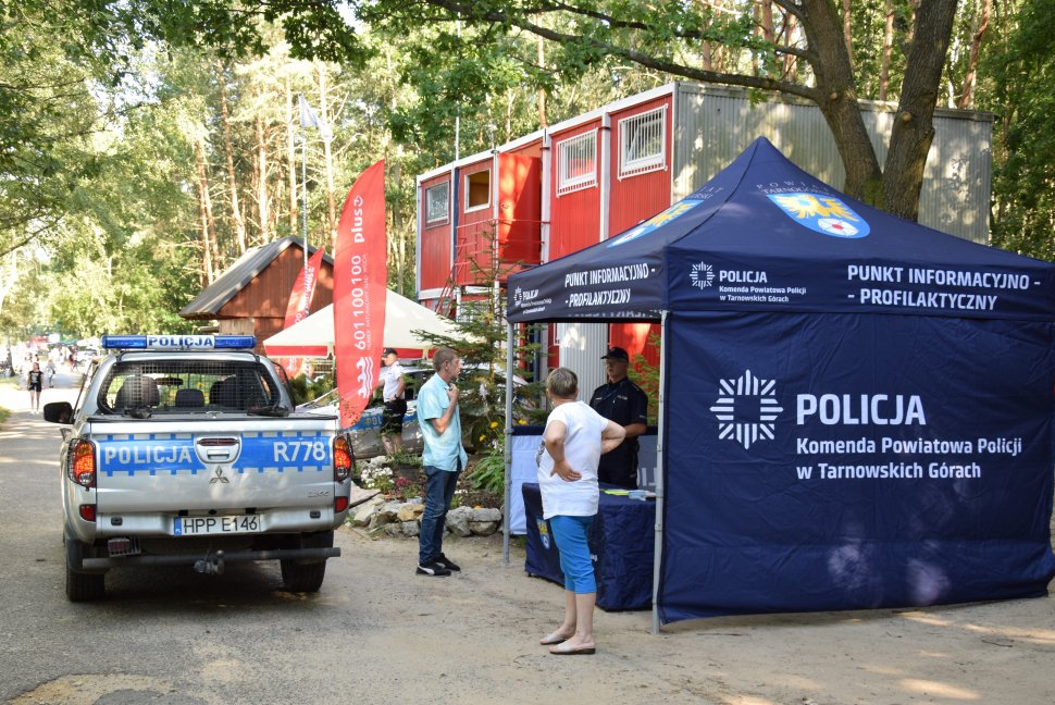 Na zdjęciu widać policyjny punkt informnacyjno - profilaktyczny  wewnątrz, którego stoi policjant, a obok przechodnie. Obok namiotu widać zaparkowany samochód
