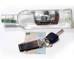 Zdjęcie przedstawia butelkę alkoholu, obok której leży dowód rejestracyjny pojazdu. Na dowodzie rejestracyjnym leżą kluczyki od samochodu.