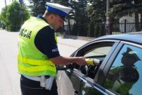 Zdjęcie przedstawia policjanta ruchu drogowego, który wykonuje badanie trzeźwości u zatrzymanego do kontroli drogowej kierowcy samochodu.