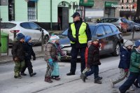 Zdjęcie przedstawia policjanta, który przeprowadza przez przejście dla pieszych grupę dzieci.