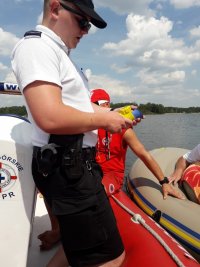 Na fotografii widać policjanta znajdującego się na łodzi, który odczytuje z urządzenia wynik badania stanu trzeźwości.