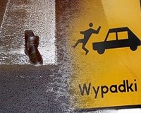 Z prawej strony fotografii widać samochód, który potrąca człowieka. Pod grafiką znajduje się napis WYPADKI. Z lewej strony fotografii widać znajdujący się na przejściu dla pieszych but.