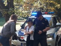 Na fotografii widać opartych o policyjny radiowóz policjanta i Miłosza. Przed nimi znajduje się kobieta, która daje chłopcy policyjnego lizaka.