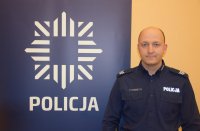 Na fotografii widać sierżanta sztabowego Pawła Zrałka, który stoi obok baneru, na którym widać policyjną gwiazdę, pod którą widnieje napis POLICJA