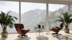 Na fotografii widać pomieszczenie bardzo dużymi  oknami, przez które rozciąga się widok na góry. Na środku  pomieszczenia widać również dwa krzesła, stolik oraz dwie doniczki z palmami.