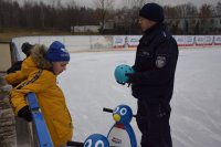 Na fotografii widać lodowisko, na którym policjant rozmawia z chłopcem stojącym przy bandzie