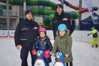 Na fotografii widać lodowisko, na którym znajdują się dwaj policjanci oraz młodzi łyżwiarze. Dziewczynka i chłopiec mają na głowach kaski narciarski, które wygrali  w konkursie.