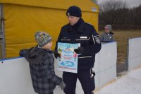 Na fotografii widać lodowisko, na którym policjant rozmawia z chłopcem stojącym przy bandzie. Mundurowy trzyma w dłoni plakat z kampanii &quot; Kręci mnie bezpieczeństwo na stoku&quot;