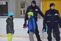 Na fotografii widać lodowisko, na którym dwaj policjanci rozmawiają z  dwoma młodymi łyżwiarzami.
