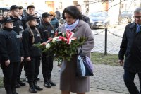 fotografia kolorowa. Posłanka na Sejm Barbara Dziuk niesie wiązankę z kwiatami, obok widać uczniów klas policyjnych