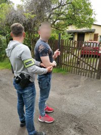 Na fotografii widać policjanta, który trzyma za rękę zatrzymanego mężczyznę. Sprawca wskazuje na dom, do którego się włamał.