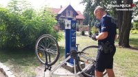 Na zdjęciu widać policjanta, który sprawdza rower między innymi jego wyposażenie i numer ramy. Rower obrócony jest kołami do góry.