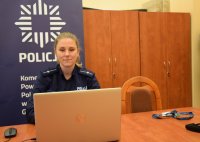 Na zdjęciu widać policjantkę, która siedzi przy stole, przed laptopem i prowadzi zajęcia profilaktyczne online.