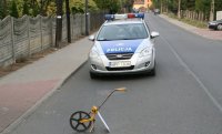 Na zdjęciu widać zaparkowany na drodze policyjny radiowóz, przed którym znajduje się urządzenie do pomiaru odległości.