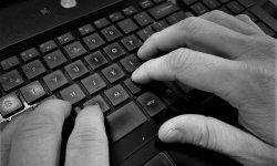 Zdjęcie czarno-białe. Na fotografii widać dłonie piszące na klawiaturze komputera.