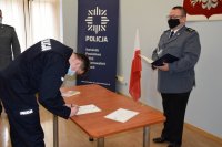 Na zdjęciu widać Komendanta Bylickiego oraz policjanta, który podpisuje dokument znajdujący się na stole.