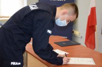 Na zdjęciu widać policjanta, który podpisuje dokument znajdujący się na stole.