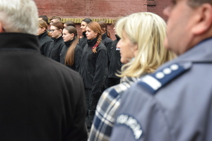 na zdjęciu fragment policyjnego munduru, w oddali klasa mundurowa stoi w dwuszeregu