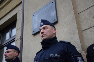na zdjęciu policjant w trakcie warty pod pamiątkową tablicą na murach komendy