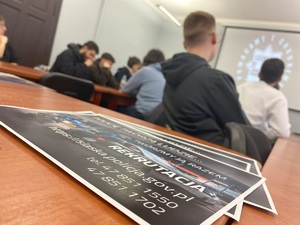 na zdjęciu ulotka informacyjna z napisem rekrutacja, z tyłu uczniowie siedzący przy stołach