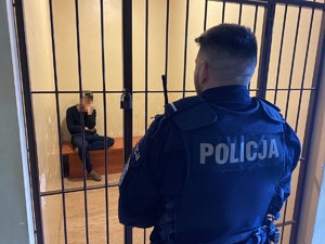 na zdjęciu zatrzymany w celi, a przed nią policjant